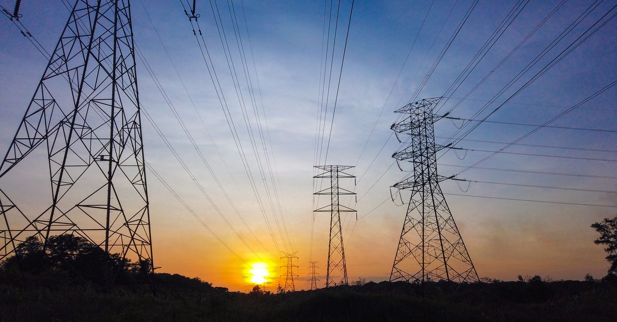 Silhouetted power lines and towers against a striking sunset sky, illustrating energy supply themes.